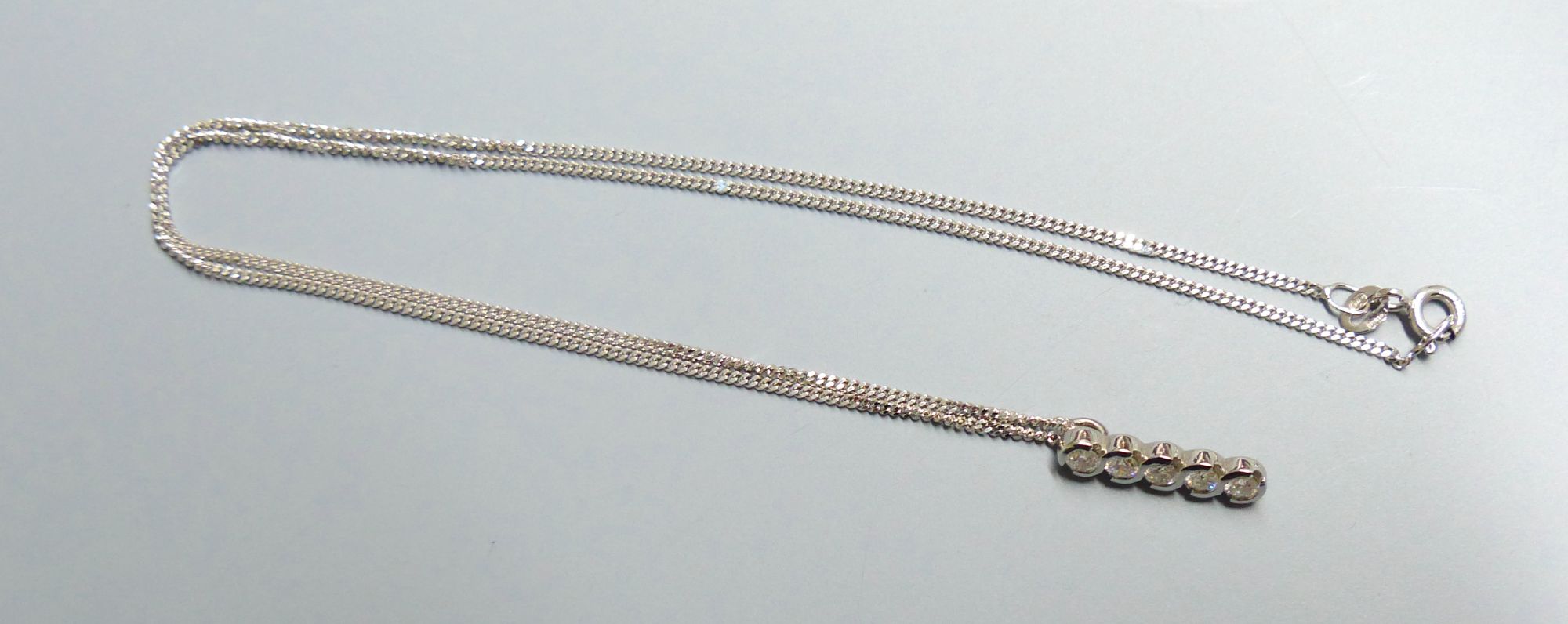 A modern 18ct white gold and five stone diamond set line pendant, on an 18ct white gold fine link chain,
